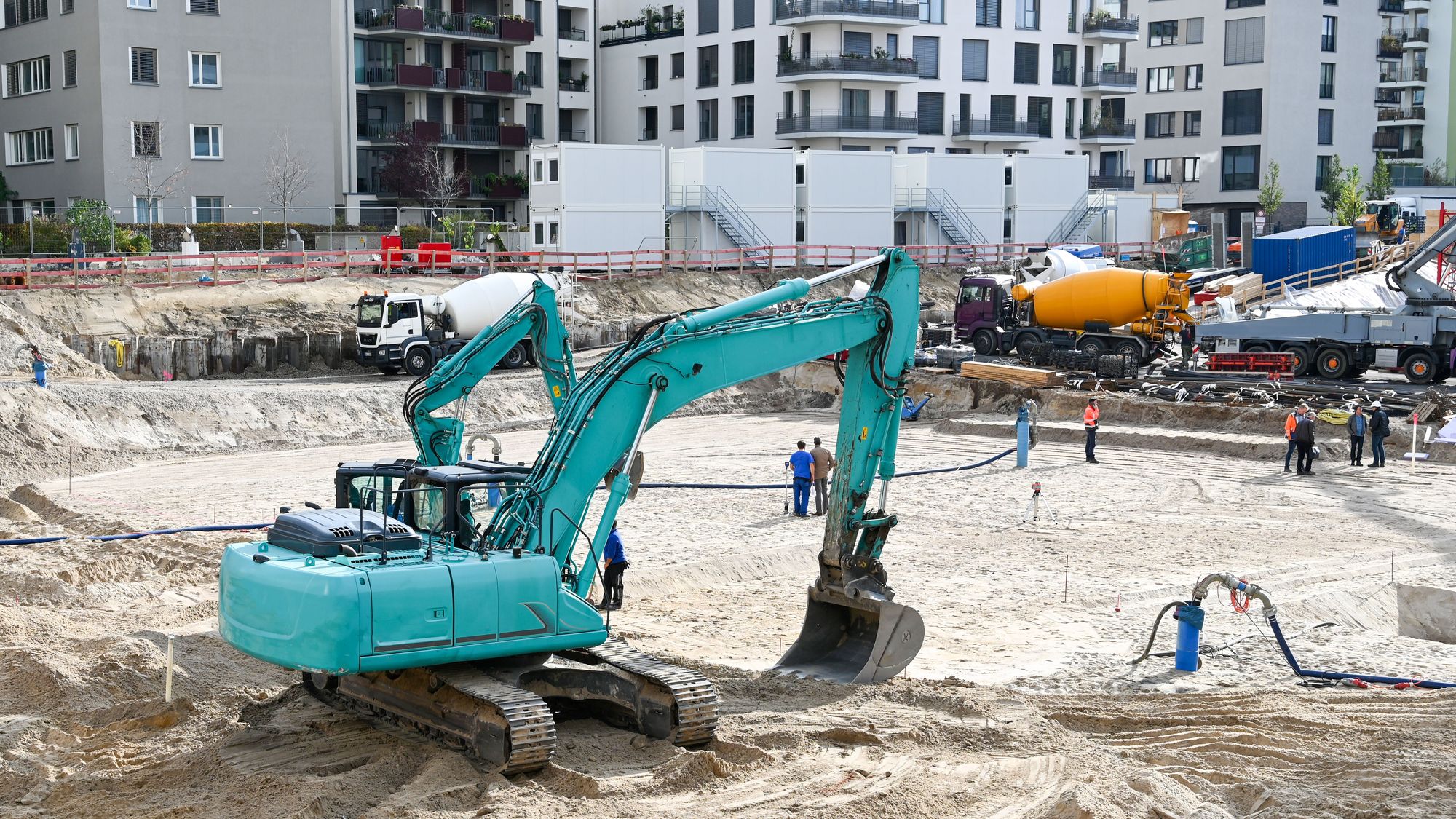 Bagger auf einer Baugrube vor neu errichteten Wohngebäuden